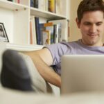Mid adult man sitting on sofa looking at laptop