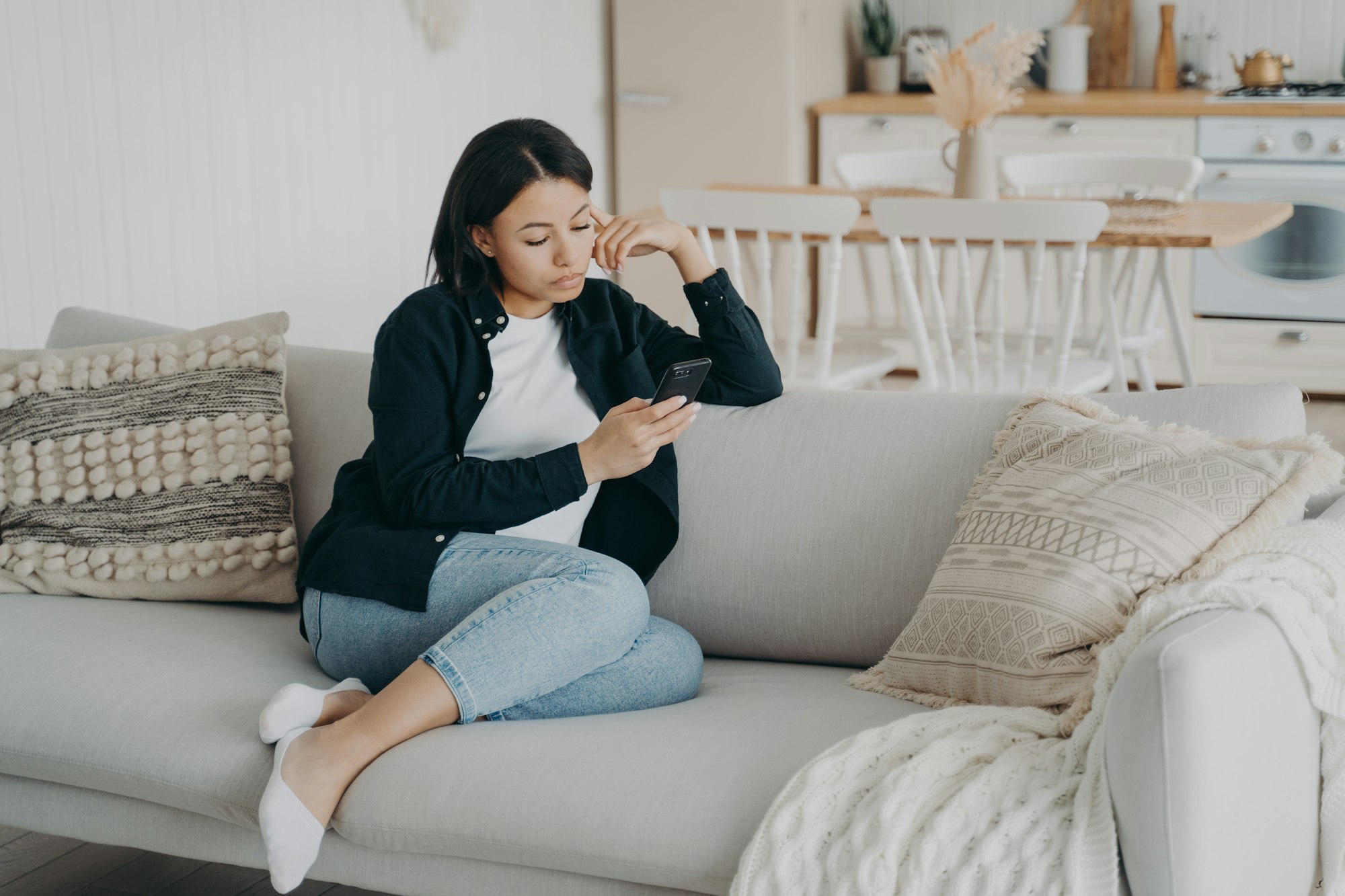 Modern female uses mobile apps at home spending leisure time online with smartphone sitting on couch