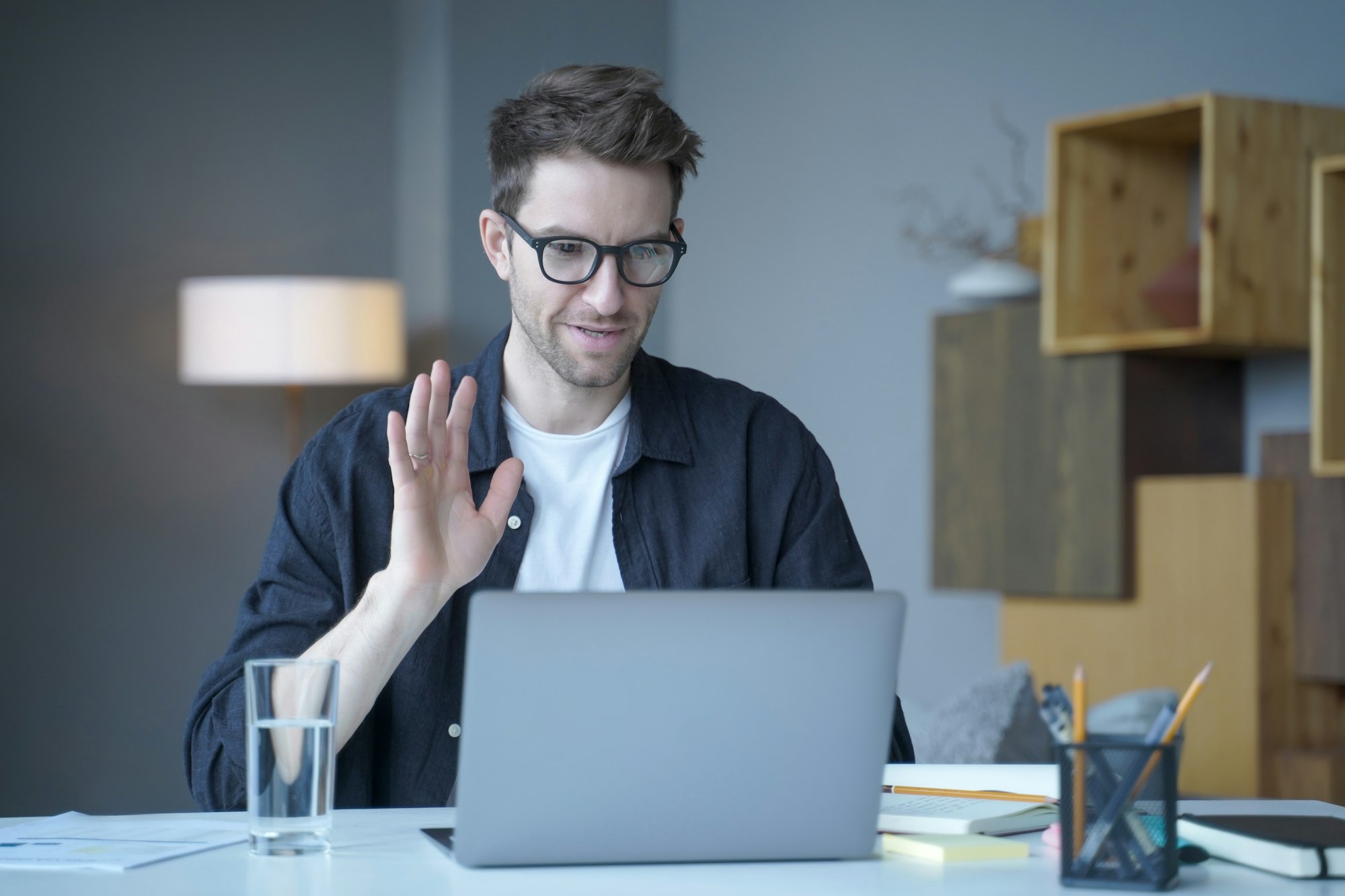 Young handsome austrian man freelancer waving hand in hello gesture during video call on laptop