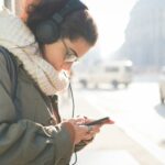 Young woman wearing headphones choosing smartphone music on street