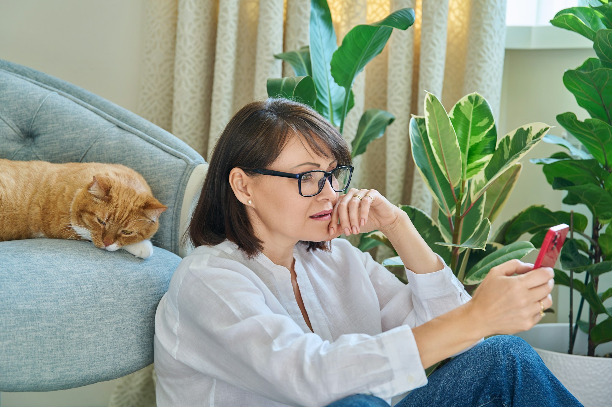 Mature woman sitting at home, using smartphone