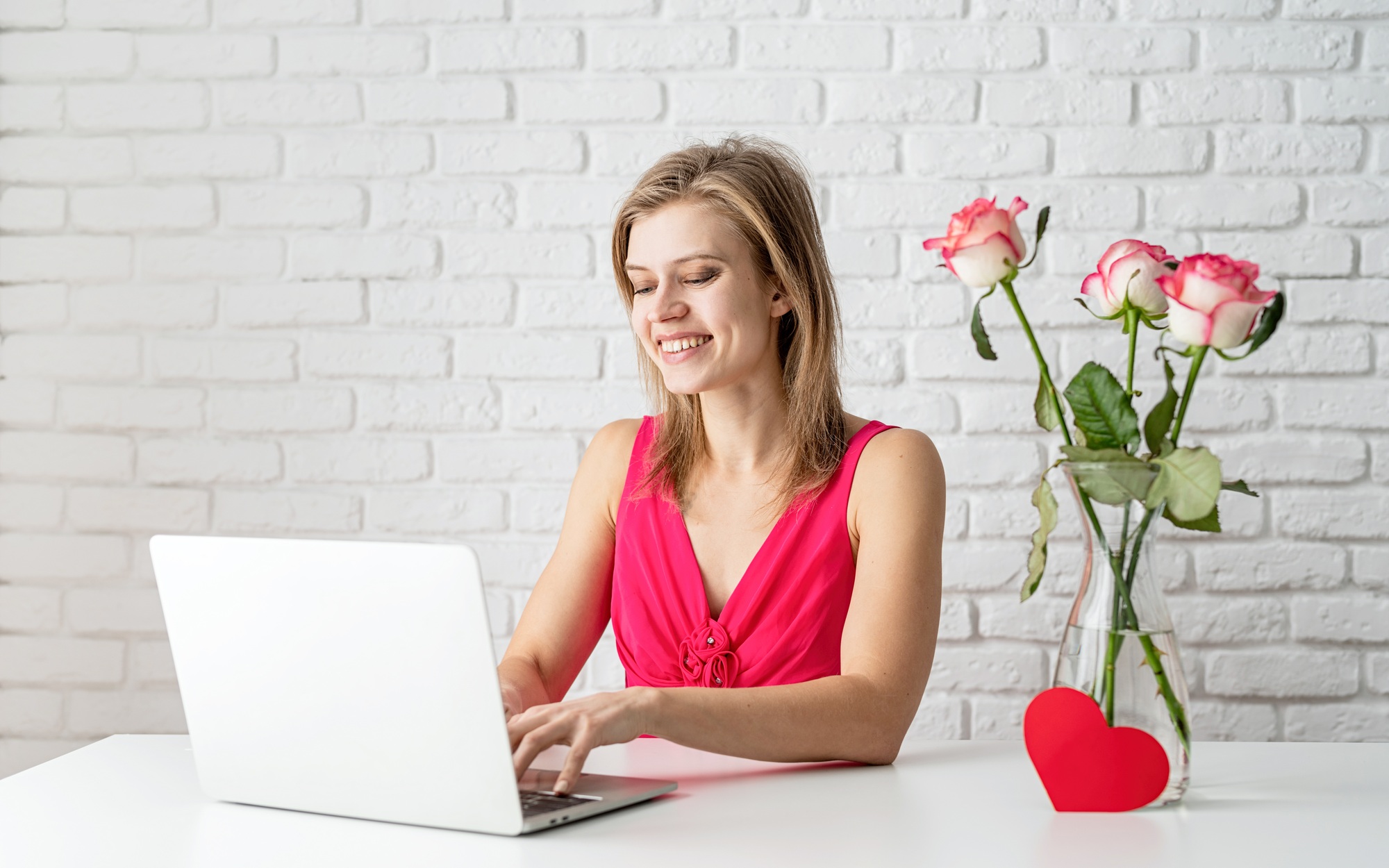 Valentines Day. Beautiful blond woman in pink dress dating online using laptop